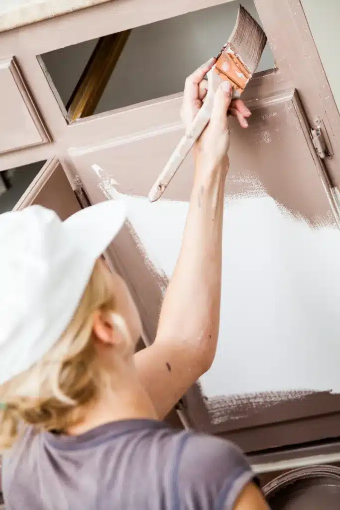 Closeup of Woman Holding Paint Brush and Painting Kitchen Cabinets. What to be Prepared for When Painting Your Cabinets